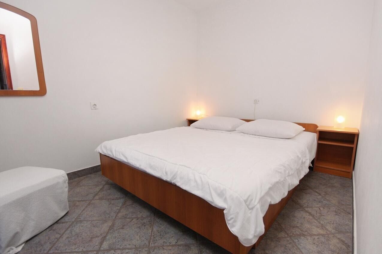 A single-bed room with a wooden frame, white bedding, two bedside tables, and a small shelf.