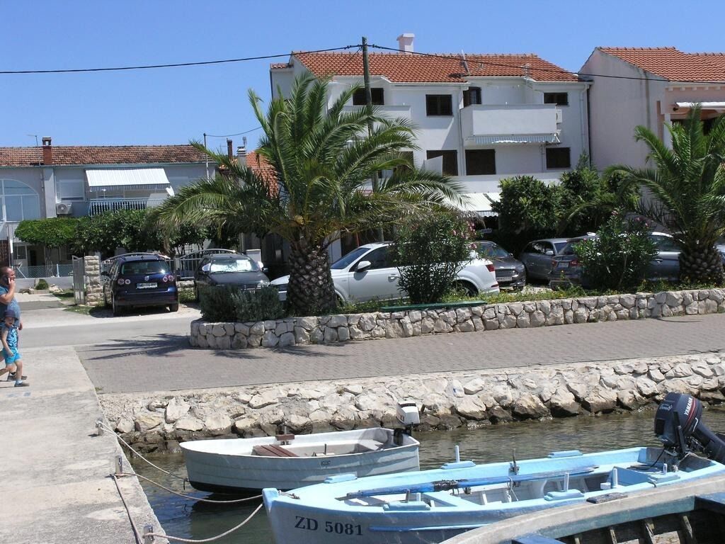 A marina with boats docked, a stone wall, and a building with a tiled roof in the background.