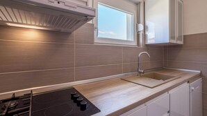 Egy modern konyha beépített tűzhellyel, a mosogató felett elhelyezett ablakkal és fehér színű konyhaszekrényekkel.