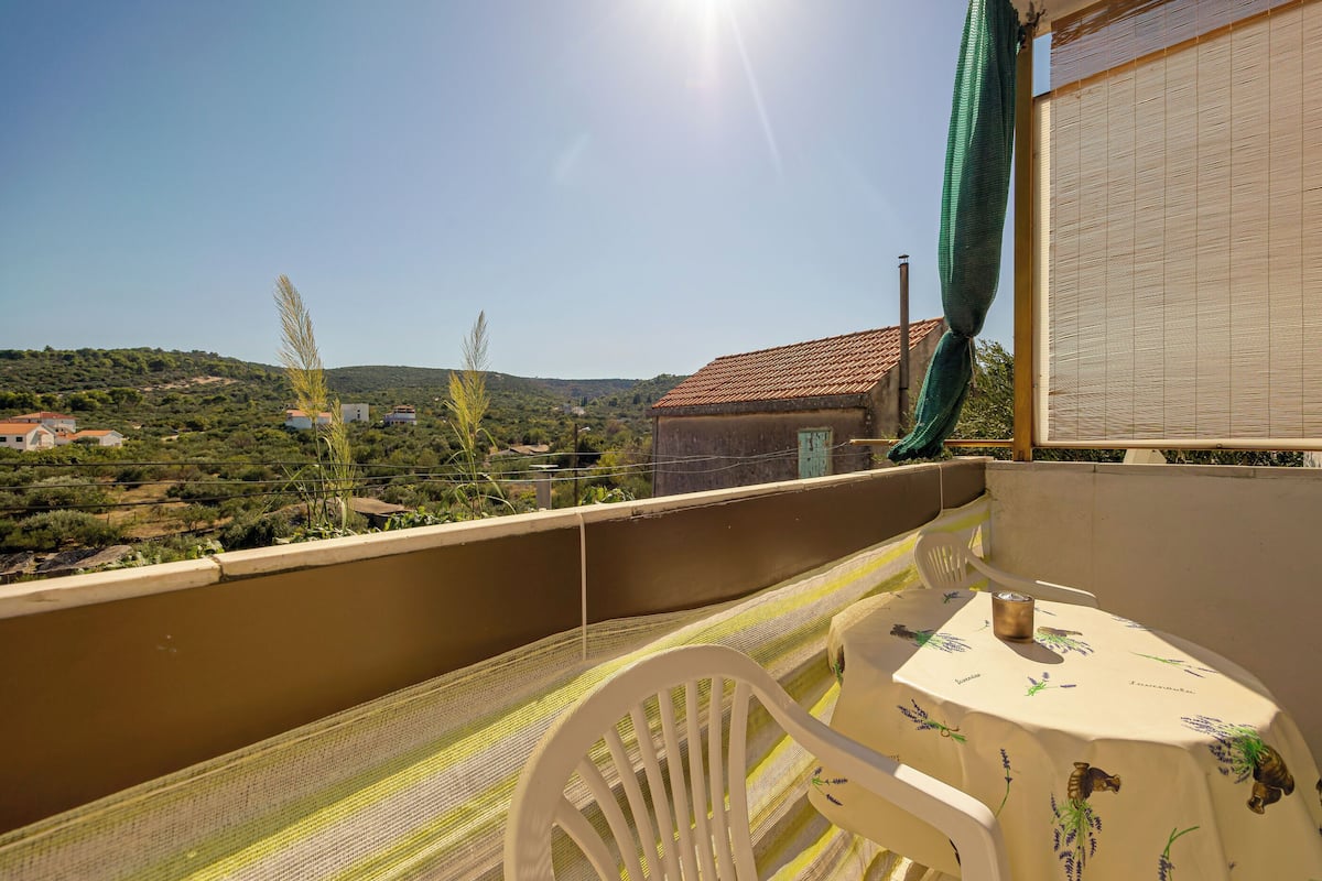 A balcony with a table and chairs, overlooking a hilly landscape.