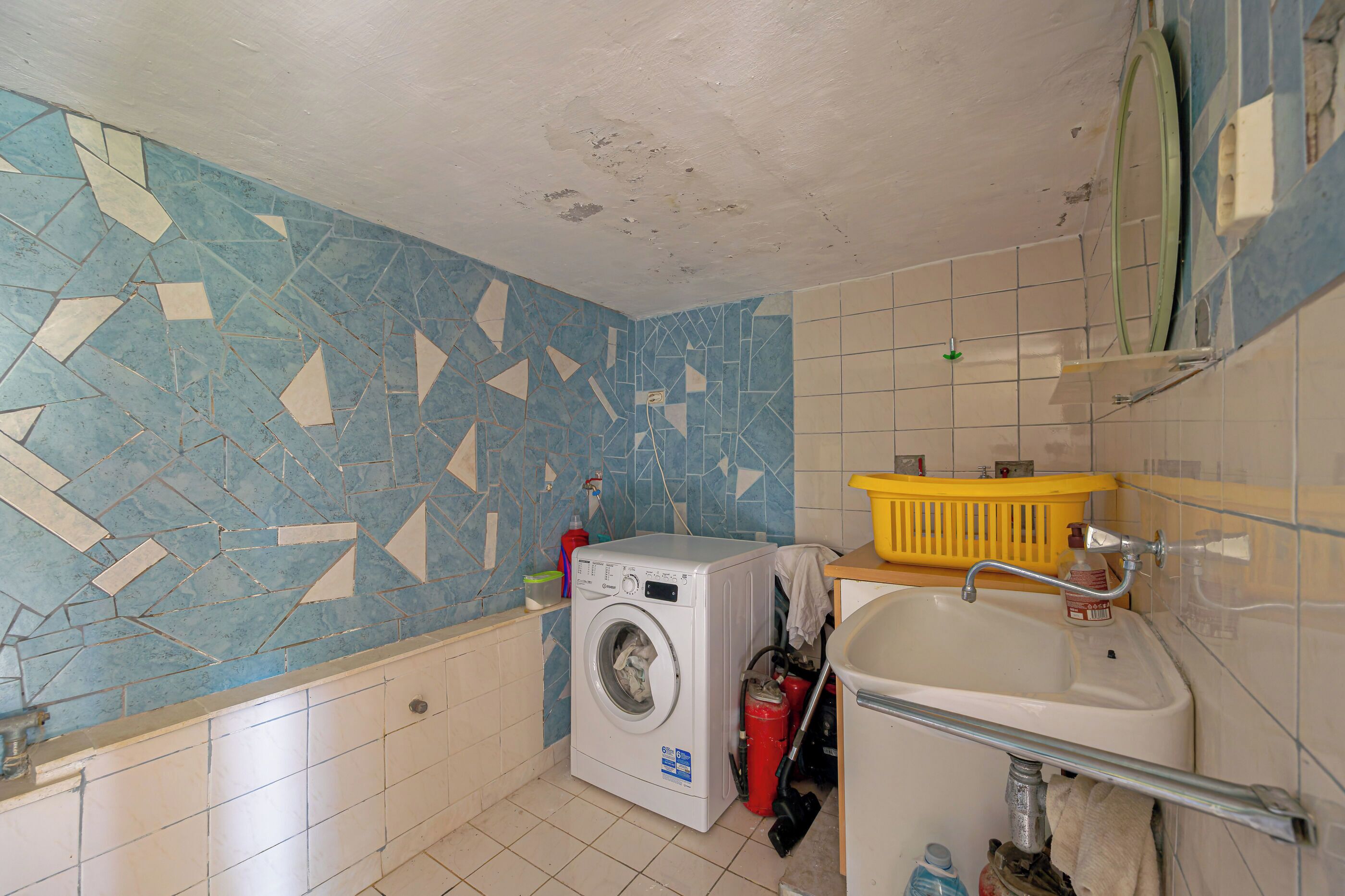 A small laundry room with a washing machine, a sink, and a yellow laundry basket.