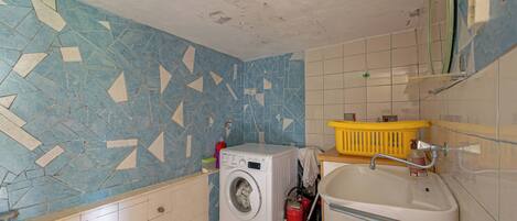 A small laundry room with a washing machine, a sink, and a yellow laundry basket.