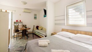 Habitación de hotel con cama, escritorio, silla, una mesita y ventana con persianas.