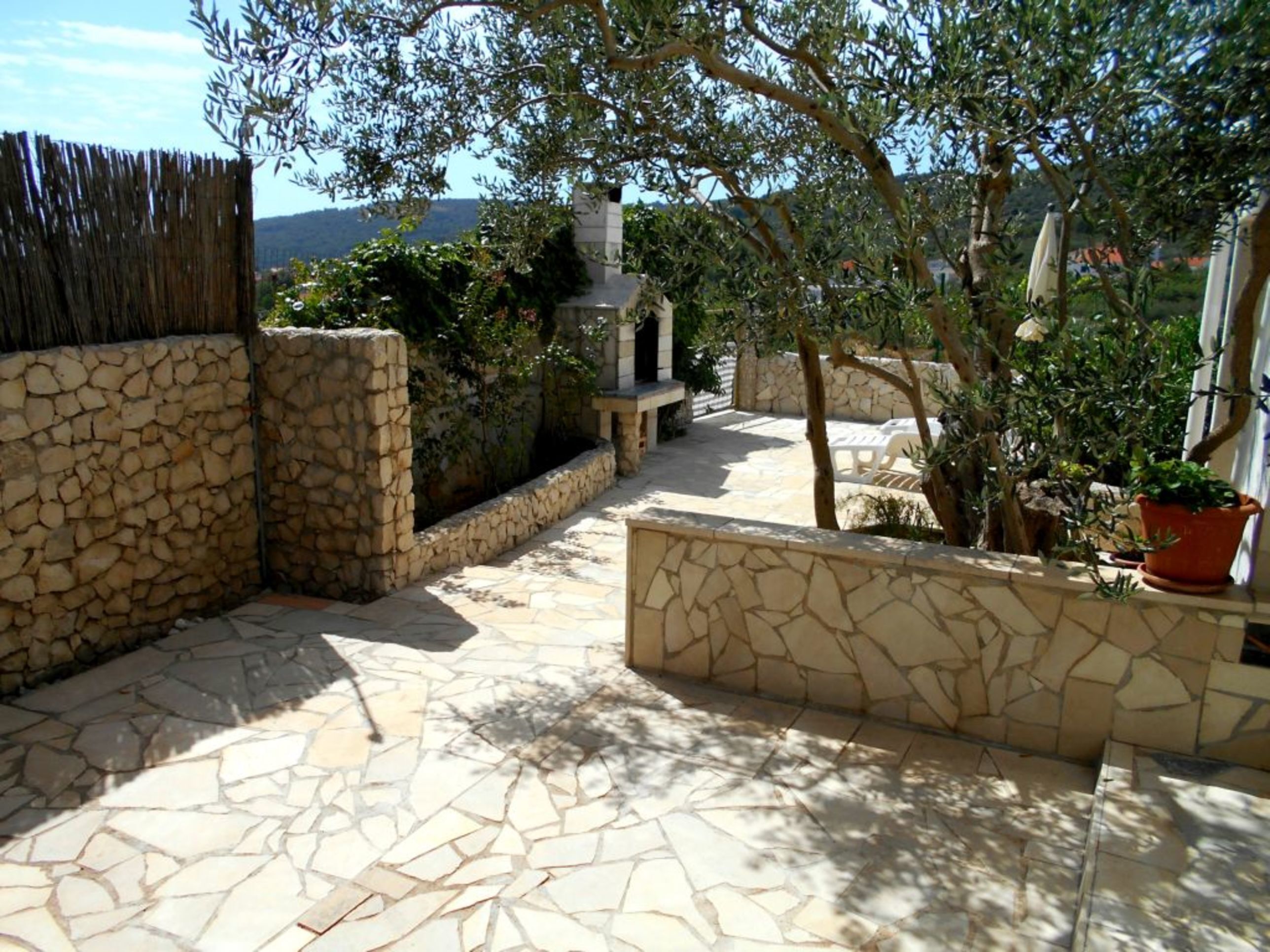 Eine Terrasse mit Steinplatten, einer Steinmauer, einem Holzzaun und Kübelpflanzen.