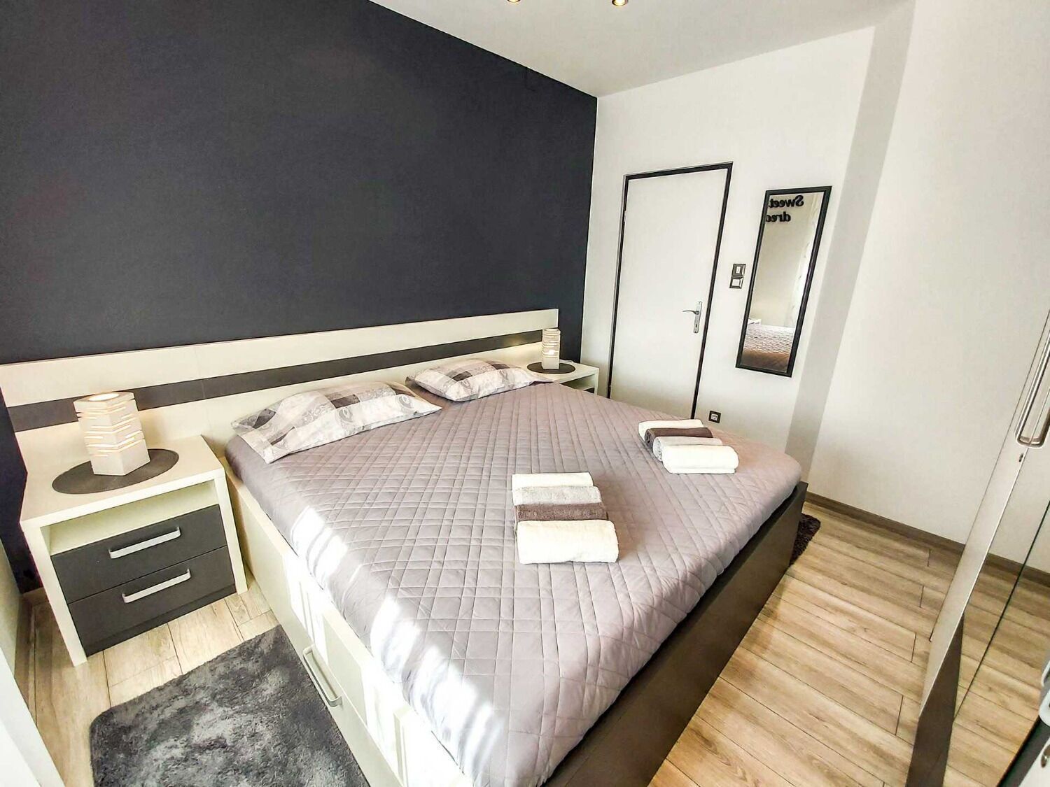 A modern bedroom with a large bed, bedside tables, a wardrobe, and a mirror.