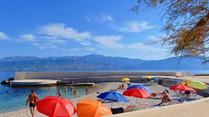 A beach with a pool, umbrellas, and people swimming and relaxing. - Apartment Vrilo (Postira)