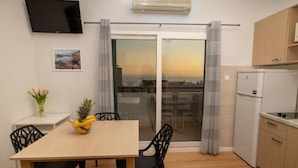 Eine kompakte Küche mit Essbereich, einem an der Wand montierten Fernseher und Blick durch die Glastür.