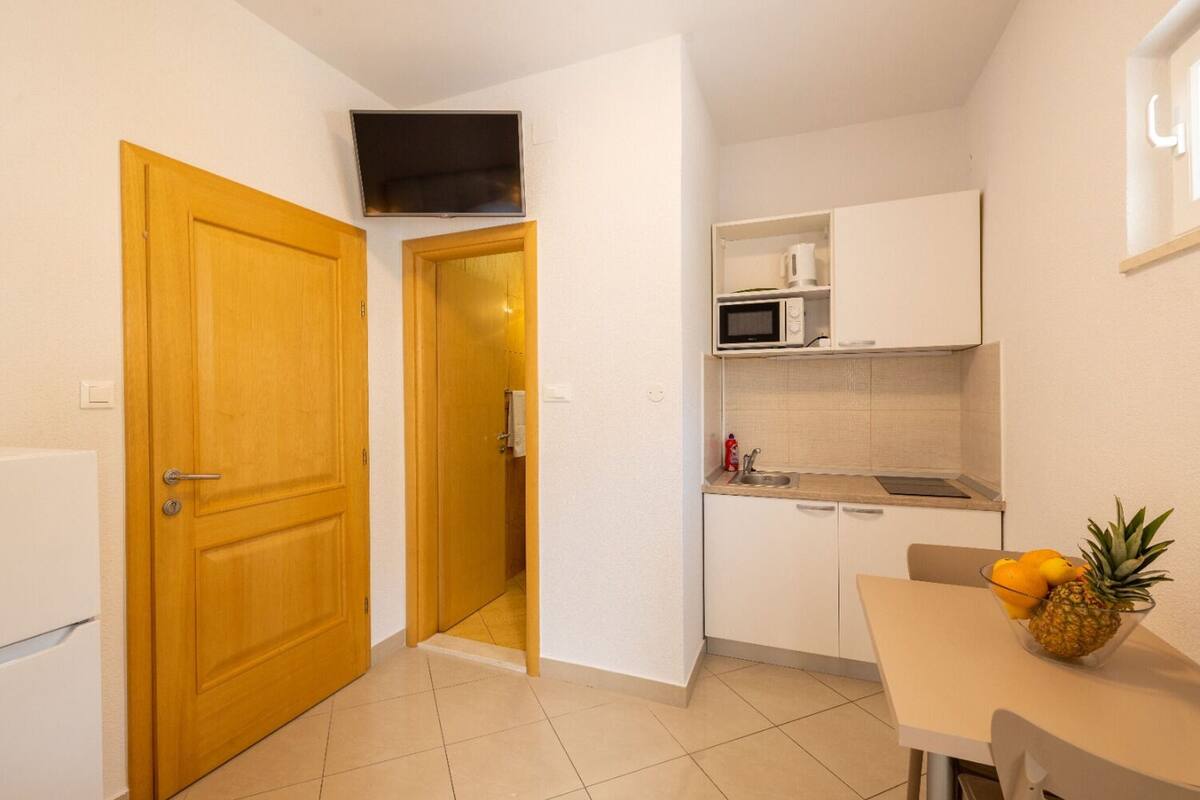 Una cucina compatta con mobili bianchi, un forno a microonde e un piccolo angolo ristoro con tavolo e sedie.