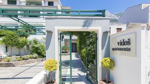 Ein befestigter Eingang zu einem Gebäude mit der Aufschrift 'vidos apartments', ein klarer Weg führt hinein.