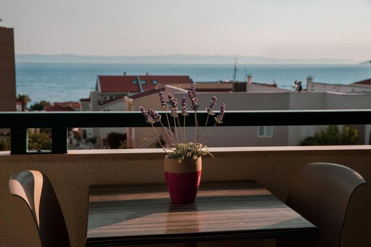 Un balcone con tavolo e sedie, una pianta di lavanda in vaso e vista sul mare e sugli edifici.