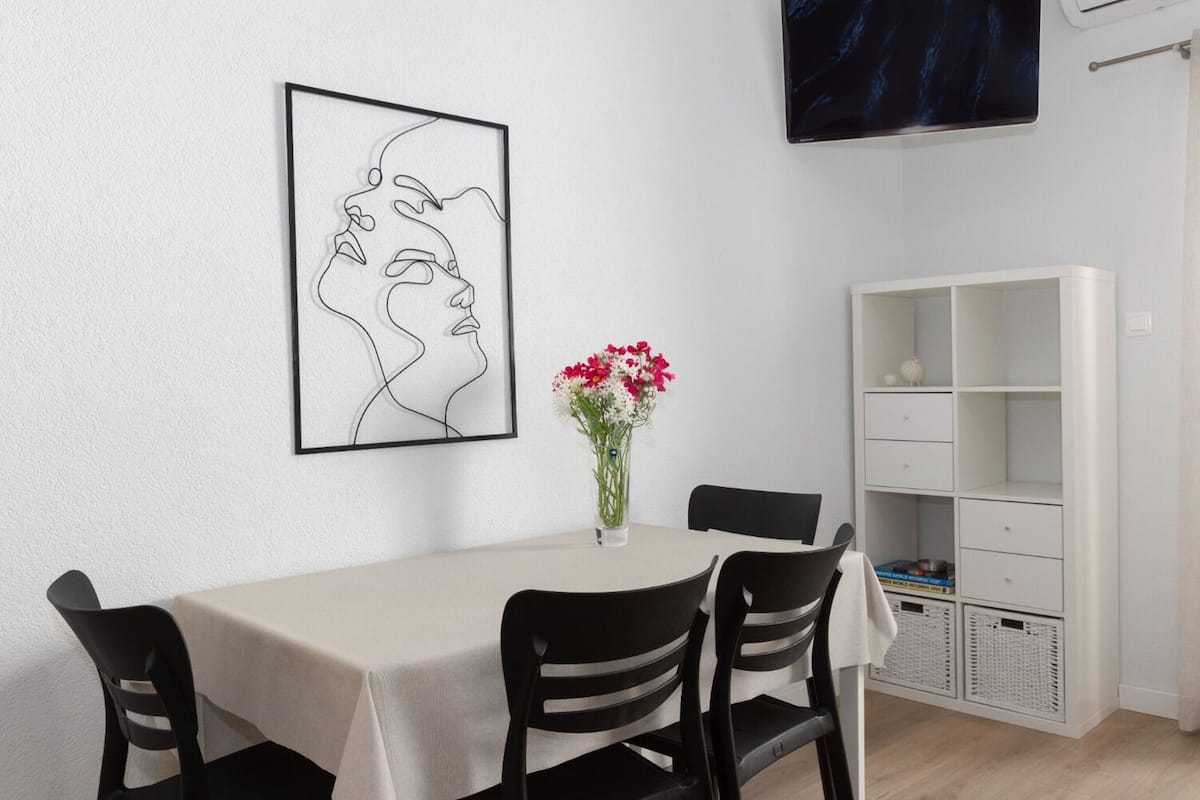 Zona pranzo con tavolo, sedie, un vaso con fiori, un'opera d'arte incorniciata e un'unità contenitore bianca.