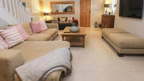 Un salon spacieux avec un haut plafond, un escalier en bois et un grand téléviseur fixé au mur.