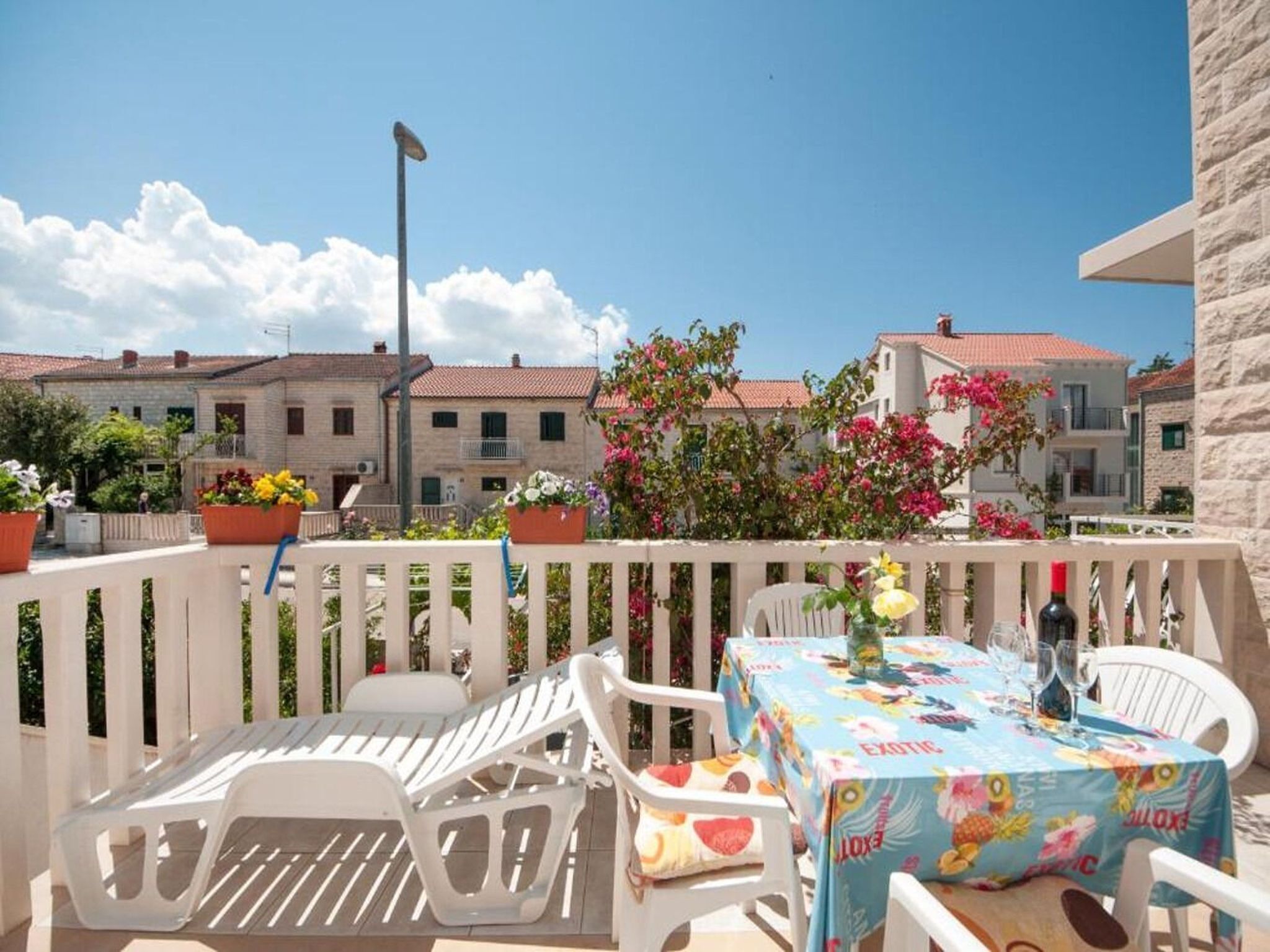 Un balcon avec des sièges d’extérieur, une table recouverte d’une nappe colorée et des plantes en pot.