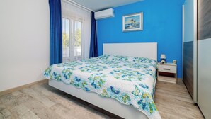 A bedroom with a bed, a nightstand, a lamp, and a painting on the wall. - Apartment Pavilion (Rab)
