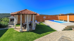 A backyard with a pergola, a swimming pool, and a barbecue area. - Apartment Pavilion (Rab)