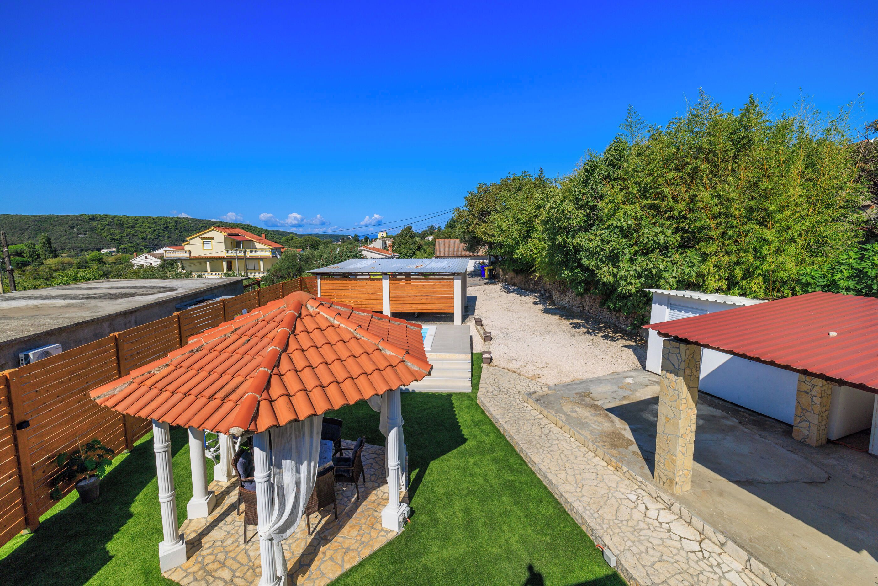 A rooftop terrace with a pergola, a stone wall, and a view of the surrounding landscape.