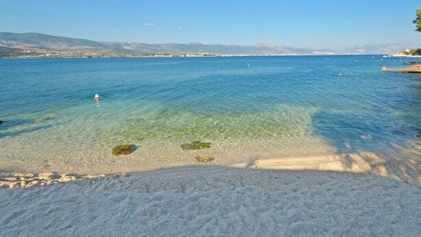 A clear beach with calm water, a sandy shore, and distant mountains. - Apartments Sima (Trogir)