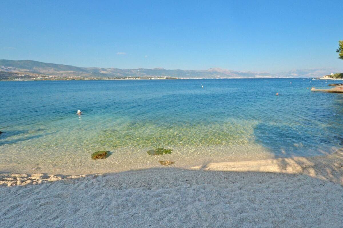 Une plage propre avec une eau calme, un rivage sablonneux et des montagnes à l’horizon.