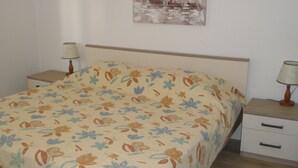 A bedroom with a floral bedspread, a wooden headboard, two bedside tables with lamps, and a wall-mounted painting. - Apartments Mateo (Primosten)
