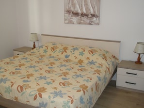 A bedroom with a floral bedspread, a wooden headboard, two bedside tables with lamps, and a wall-mounted painting. - Apartments Mateo (Primosten)