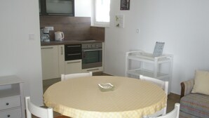 A compact kitchen with a microwave, coffee maker, and oven. There is a dining table with chairs and a small sofa in the living area. - Apartments Mateo (Primosten)