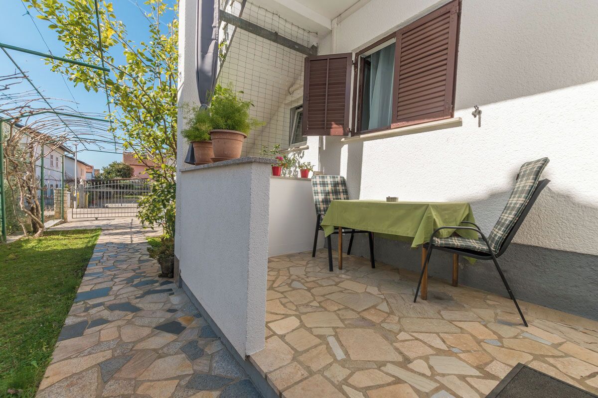 Een terras met een tafel, stoelen, potplanten en een pad van stenen.