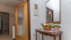A hallway with a wooden door, a mirror, a wicker basket with flowers, and a small potted plant on a wooden table. - Apartment Neva (Novigrad)