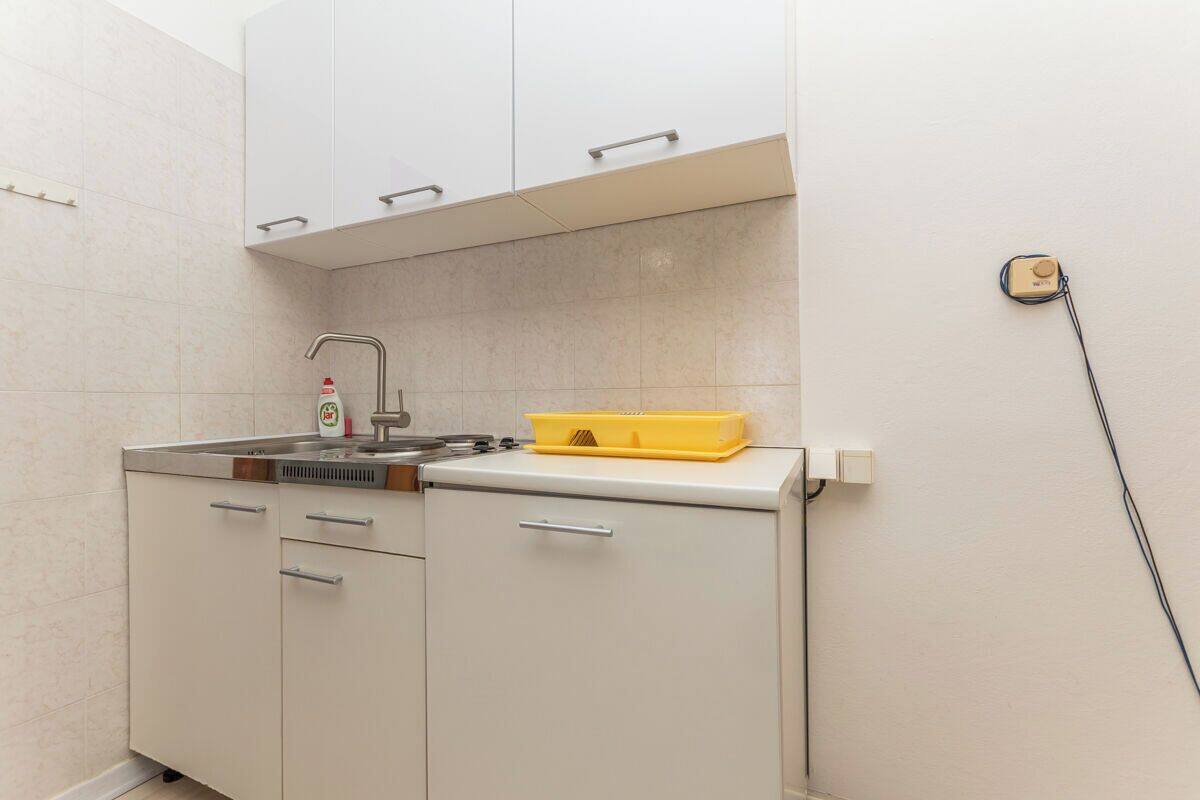 A compact kitchen with white cabinets, a sink, and a yellow tray on the countertop.