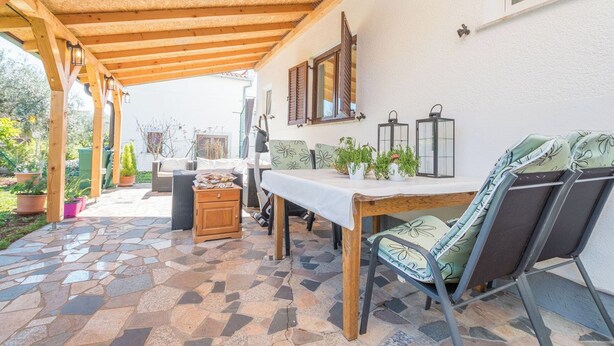 A covered patio area with a stone-tiled floor, wooden furniture, and potted plants. - Apartment Neva (Novigrad)