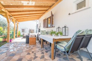 A covered patio area with a stone-tiled floor, wooden furniture, and potted plants. - Apartment Neva (Novigrad)