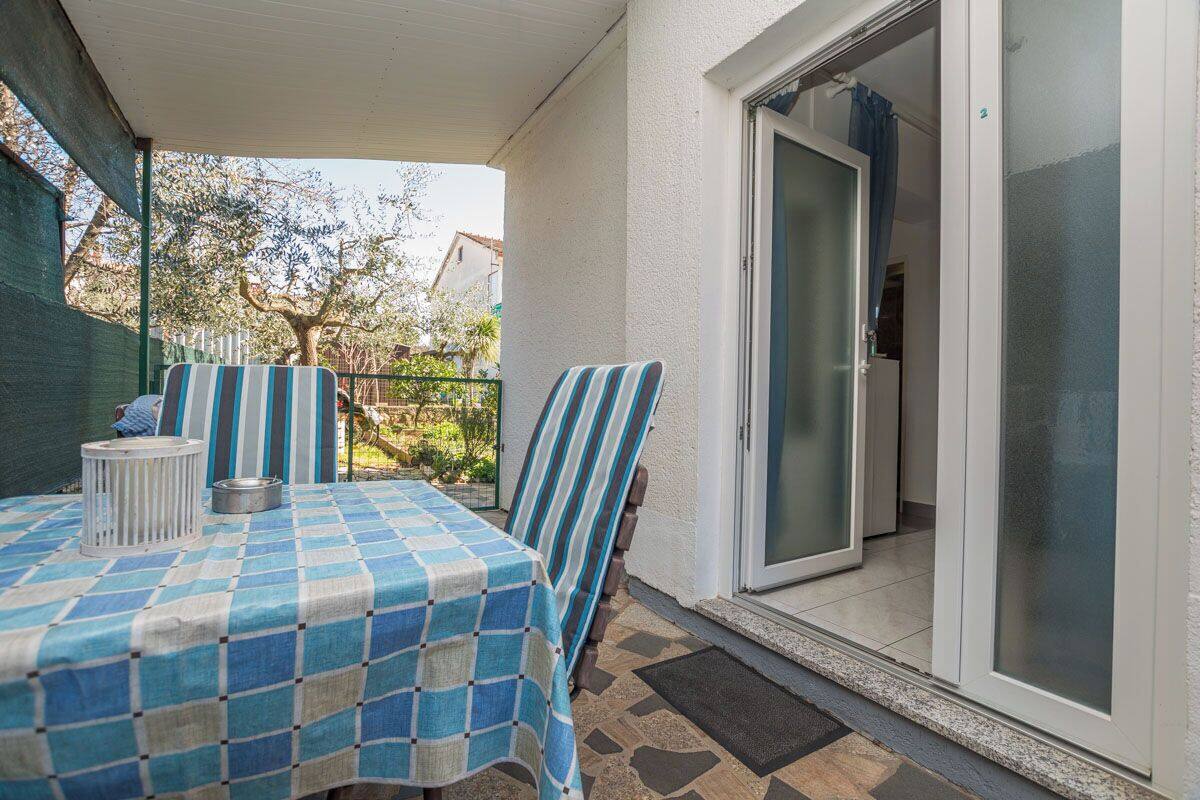 A covered patio area with a table and chairs, a sliding glass door, and a view of the surrounding garden.
