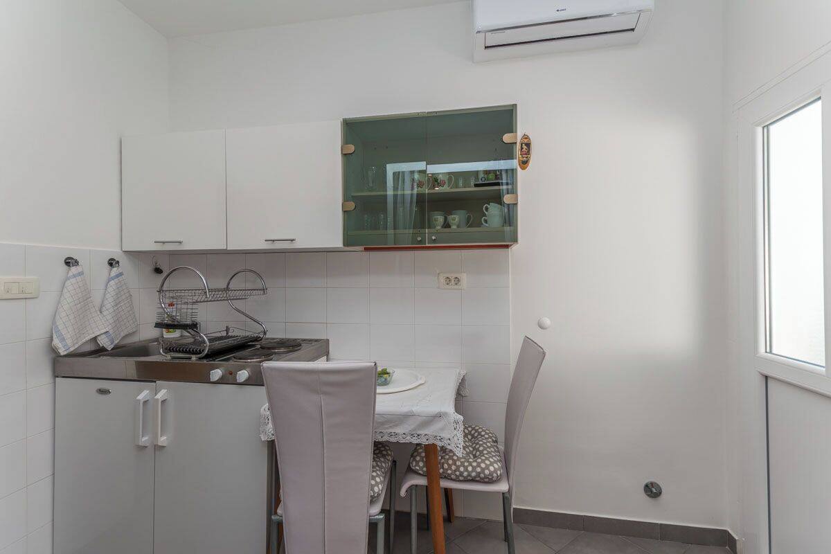 A compact kitchen with white cabinets, a built-in stove, and a small dining table with chairs.