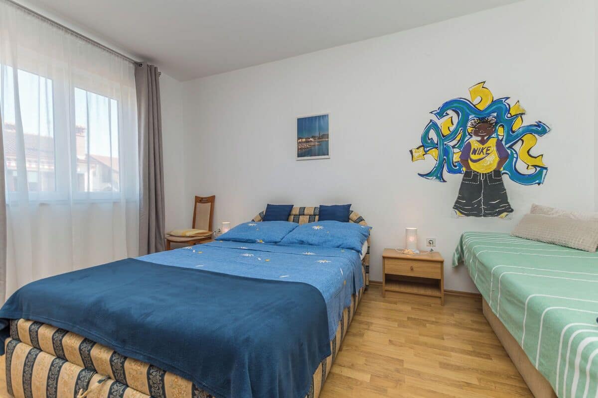 A bedroom with a large bed, a smaller bed, a nightstand, a lamp, and a wall decoration.