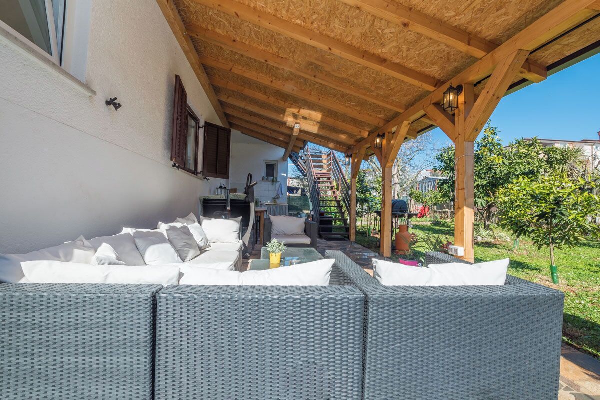 Un espace extérieur aménagé, abrité et doté de meubles en osier et d’une pergola en bois.
