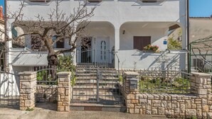 A two-story house with a stone staircase leading to the entrance, a metal gate, and a tree in the foreground. - Apartment Neva (Novigrad)