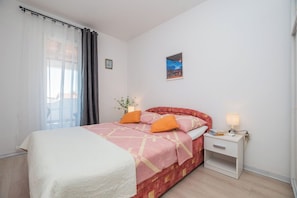 A bedroom with a bed, a nightstand, a lamp, a picture on the wall, and a window with curtains. - Apartment Neva (Novigrad)