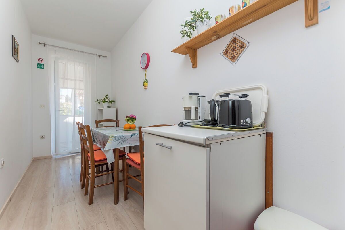 A compact kitchen with a dining table, chairs, a refrigerator, and a coffee machine.