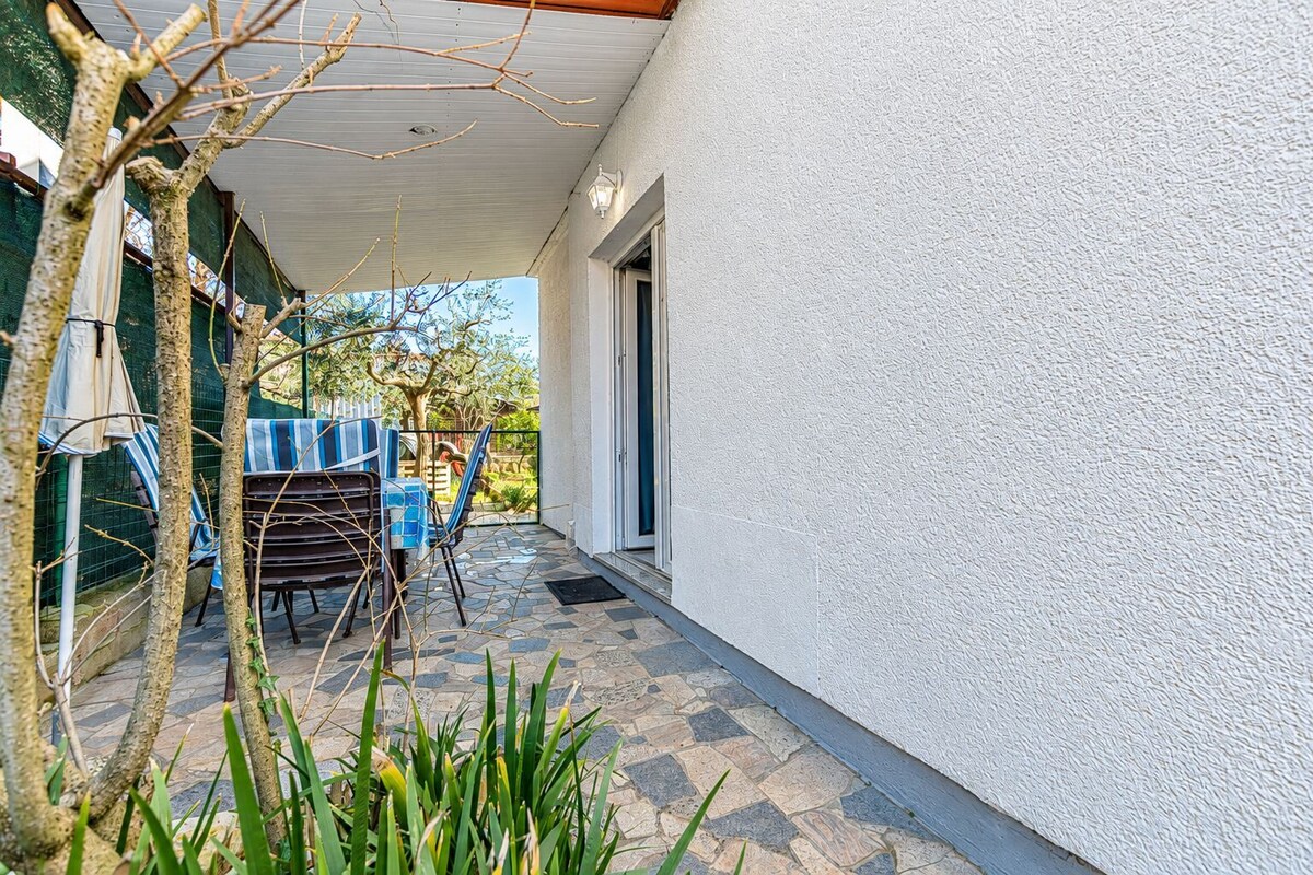 Une terrasse extérieure couverte, avec une table et des chaises, une porte et un mur blanc.