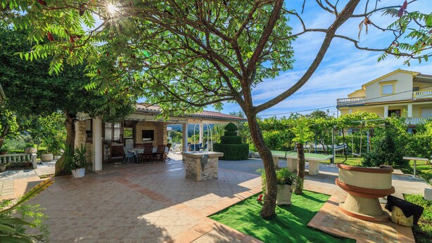 A patio area with a covered seating area, a stone table, and a well-maintained lawn. - Apartments Ankica (Rab)