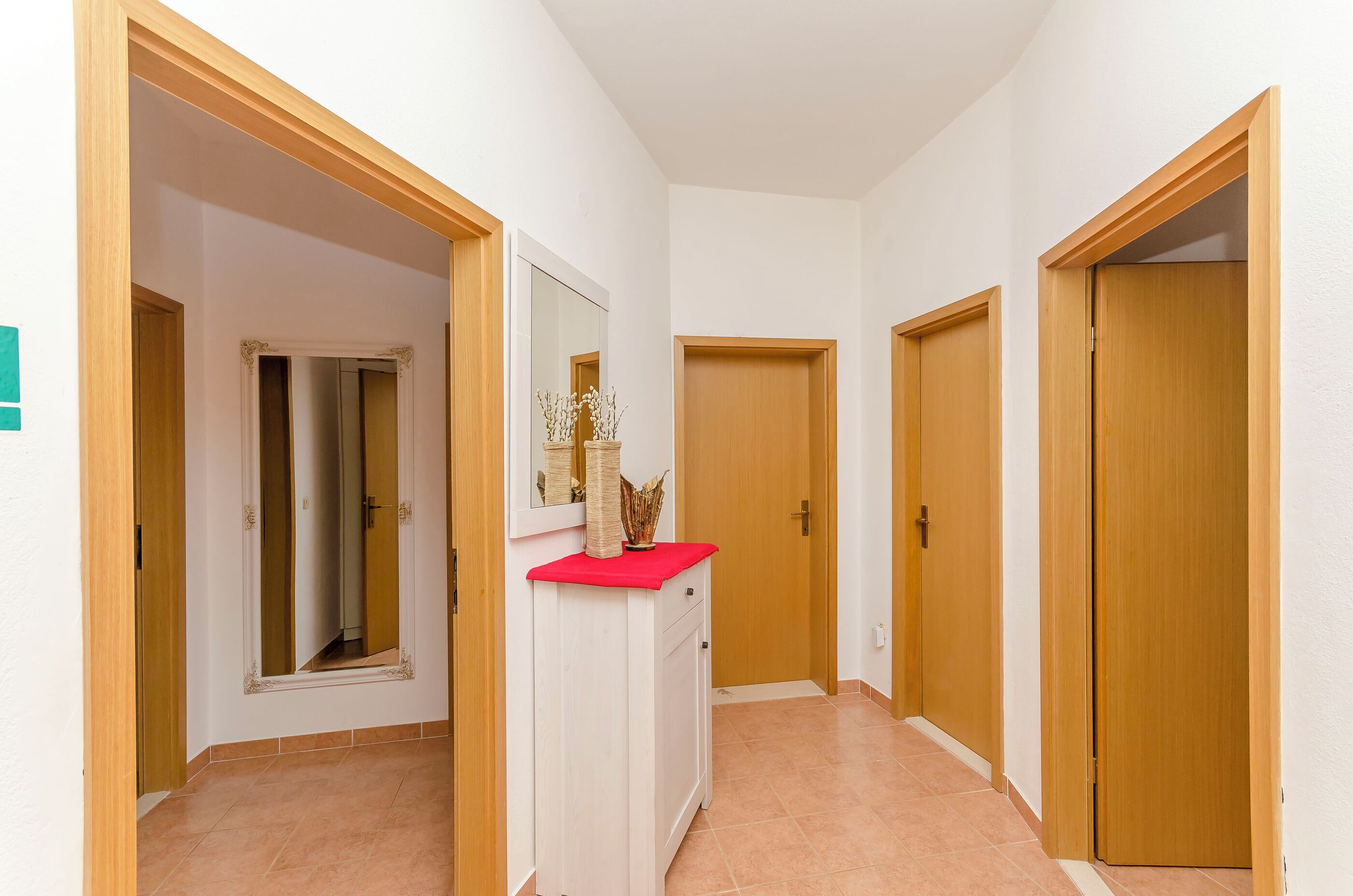 A hallway with wooden doors, a white wall, and a red countertop with a vase.