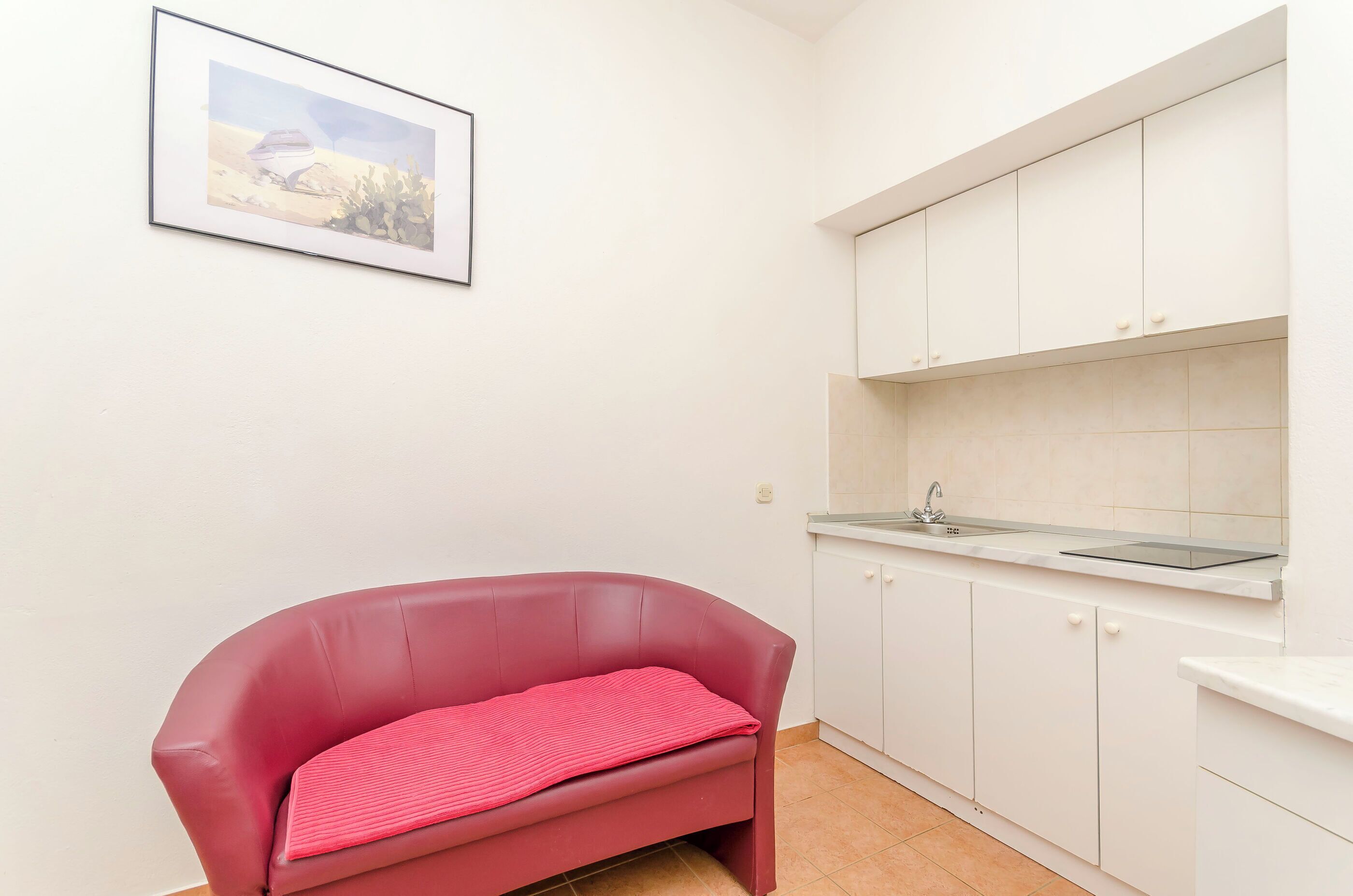 A compact kitchen with white cabinets, a sink, and a red sofa.