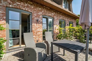 A brick building with large windows, wicker chairs, and a table outside. - Apartment 'Mama Sluuth' with Shared Terrace, Garden and Wi-Fi (Pellworm)