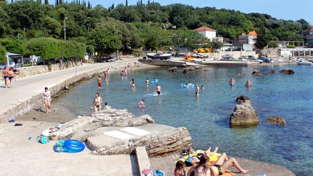 A coastal area with a rocky shoreline, clear water, and a few people swimming and relaxing. - Apartment Iva (Konavle)