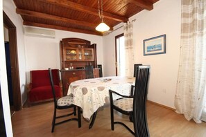 A dining area with a wooden ceiling, a table with a patterned tablecloth, and chairs. - Apartment Iva (Konavle)