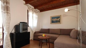A living room with a sofa, a small table with fruit, a television on a stand, a painting on the wall, and a lamp. - Apartment Iva (Konavle)