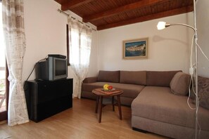 A living room with a sofa, a small table with fruit, a television on a stand, a painting on the wall, and a lamp. - Apartment Iva (Konavle)