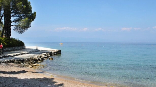Una spiaggia con un molo roccioso e una vista limpida sul mare.
