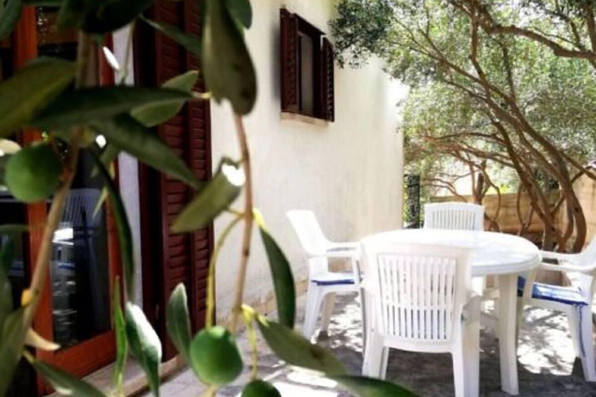 An outdoor seating area with white plastic chairs and a table, surrounded by a white wall and a tree.