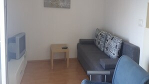 A living room with a grey sofa, a small wooden table, and a television on a stand. - Apartments Kate (Gradac)