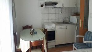 A compact kitchen with white cabinets, a stove, a sink, and a dining table with chairs. - Apartments Kate (Gradac)